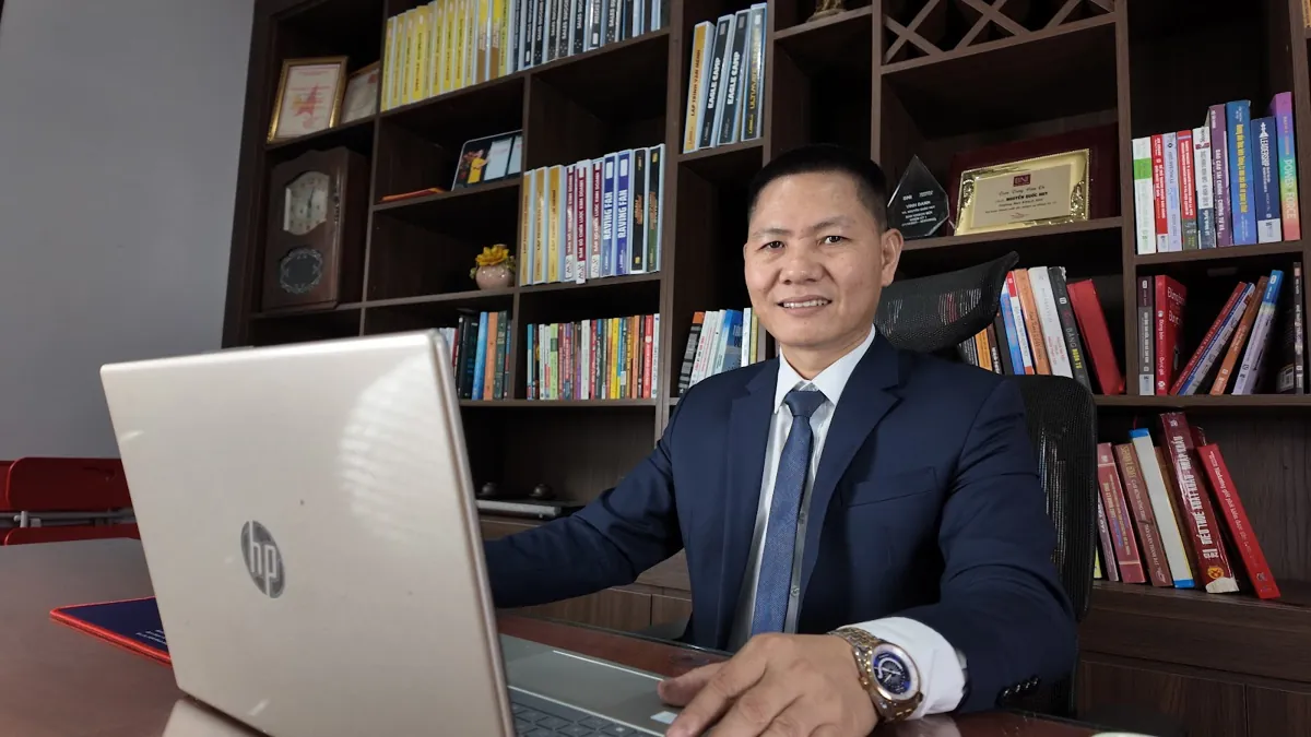 Anh Nguyễn Quốc Huy ngồi làm việc với laptop trước tủ sách tại Tâm - Tầm - Tài – Báo cáo tài chính năm
