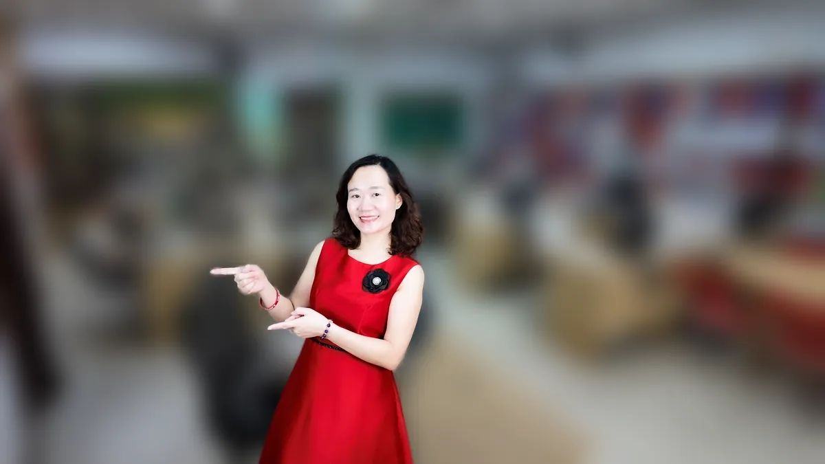 Thảo váy đỏ đưa tay như giới thiệu, mỉm cười tại văn phòng Tâm - Tầm - Tài tại văn phòng Tâm - Tầm - Tài