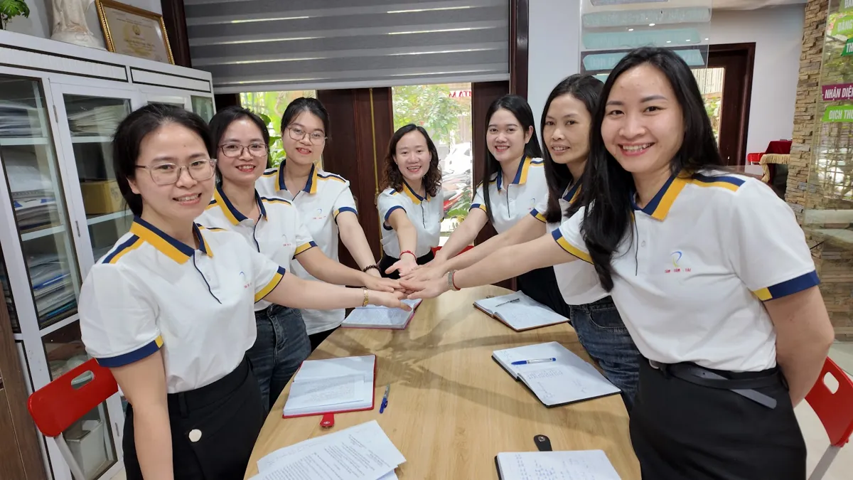 Nhân viên đồng phục chụm tay giữa bàn họp, cười tươi tại Tâm - Tầm - Tài – Đăng ký hộ kinh doanh ở đâu