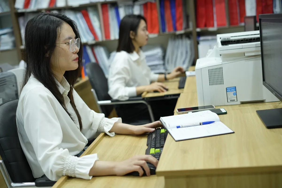 Nữ nhân viên áo trắng gõ máy tính cạnh sổ ghi chép tại Tâm - Tầm - Tài – Khai thuế hộ kinh doanh dạy thêm