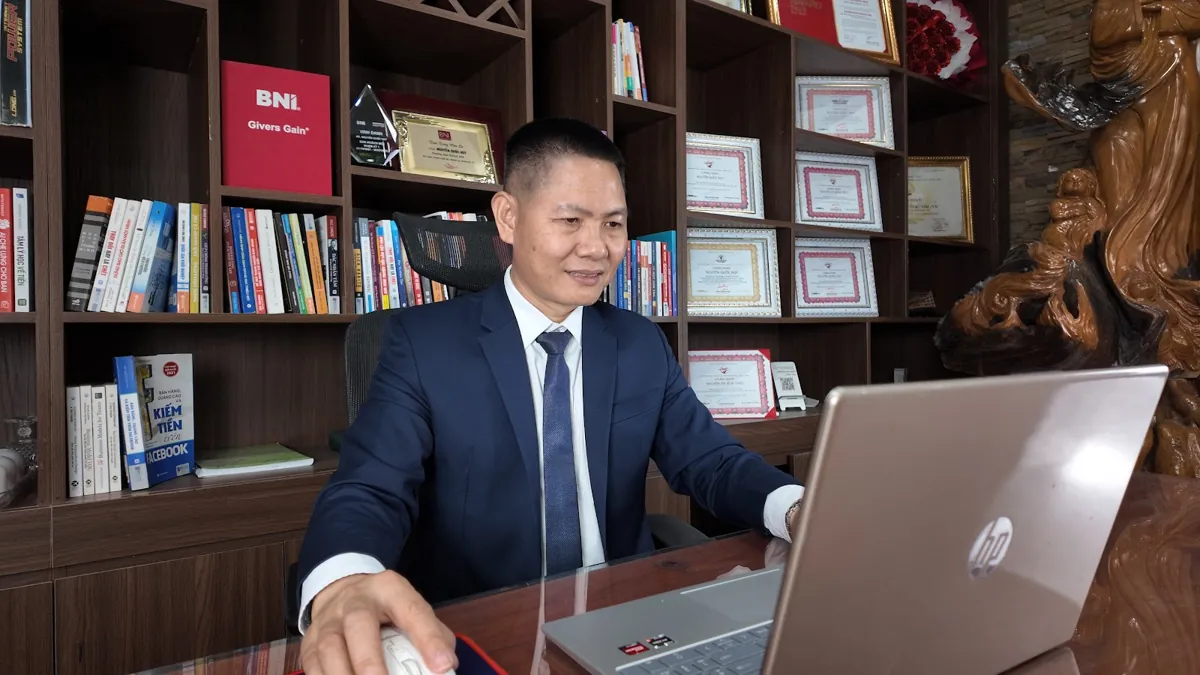Anh Nguyễn Quốc Huy dùng laptop, kệ sách và giấy khen phía sau tại Tâm - Tầm - Tài – Nâng tầm doanh nghiệp nhỏ
