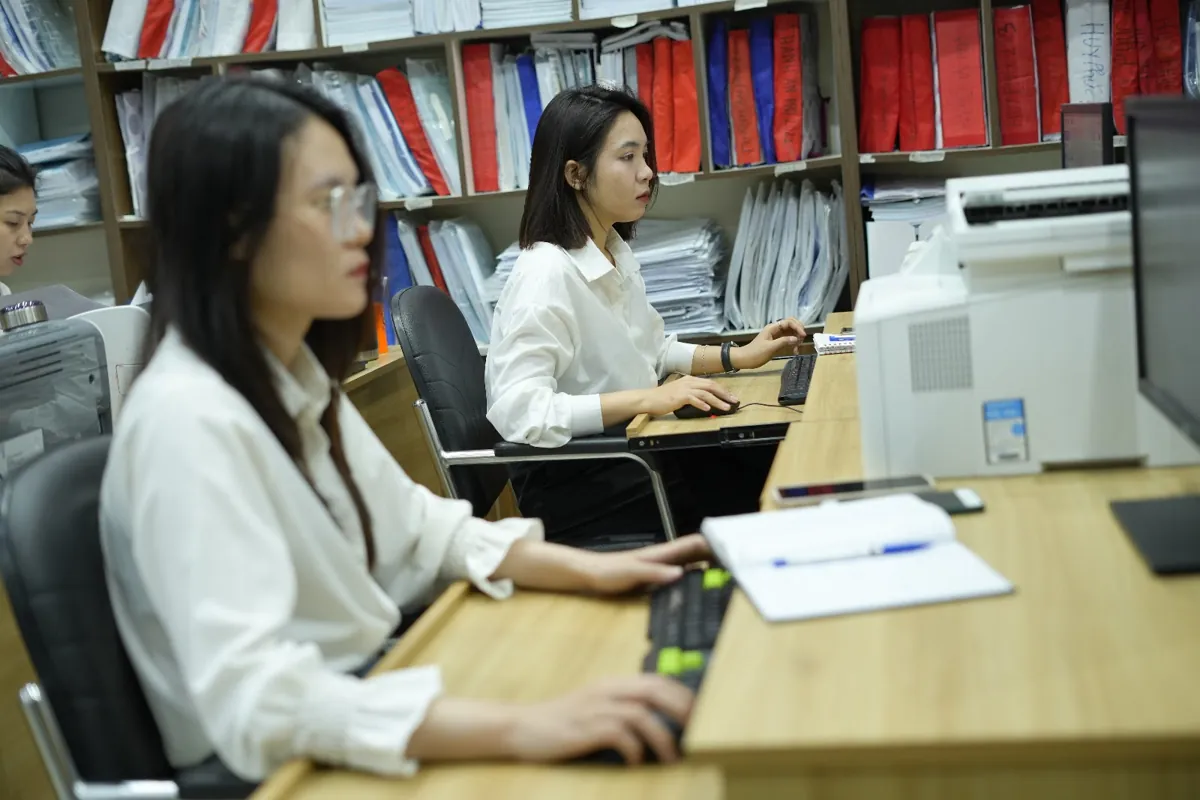 Nữ nhân viên áo trắng gõ máy tính cạnh sổ ghi chép tại Tâm - Tầm - Tài – Thủ tục mở trung tâm ngoại ngữ