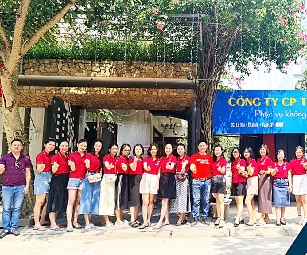 Tập thể nhân viên Tâm - Tầm - Tài trước biển hiệu công ty