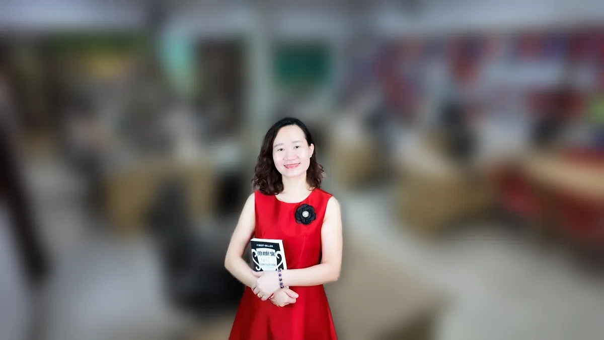 Thảo váy caro đỏ đưa hai tay như giới thiệu, mỉm cười tại văn phòng Tâm - Tầm - Tài tại văn phòng Tâm - Tầm - Tài