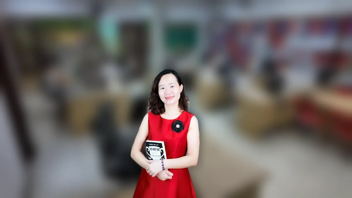 Thảo váy caro đỏ đưa hai tay như giới thiệu, mỉm cười tại văn phòng Tâm - Tầm - Tài tại văn phòng Tâm - Tầm - Tài