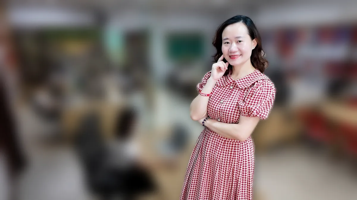 Thảo váy caro đứng nghiêng, tay đặt cằm mỉm cười tại văn phòng Tâm - Tầm - Tài tại văn phòng Tâm - Tầm - Tài