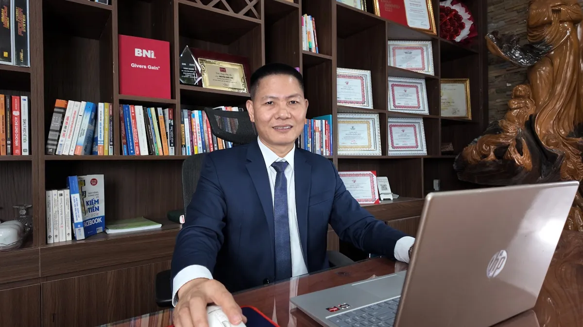 Anh Nguyễn Quốc Huy dùng laptop, kệ sách và giấy khen phía sau